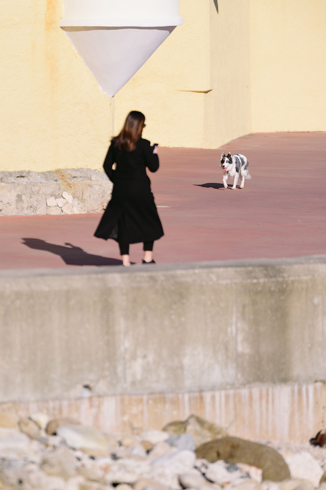 Woman in the black coat and the dog walking along the coast in Oeiras, Portugal