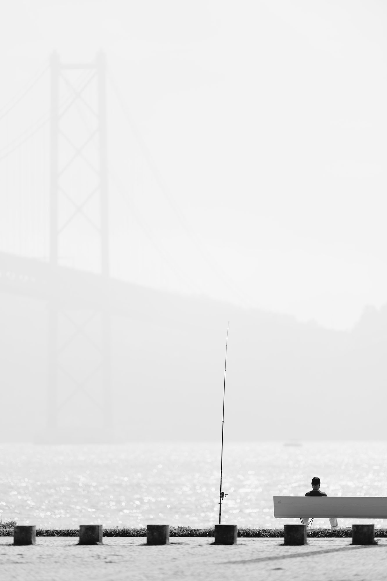 Fisherman and the 25 de Abril Bridge in Alcantara area of Lisbon, Portugal