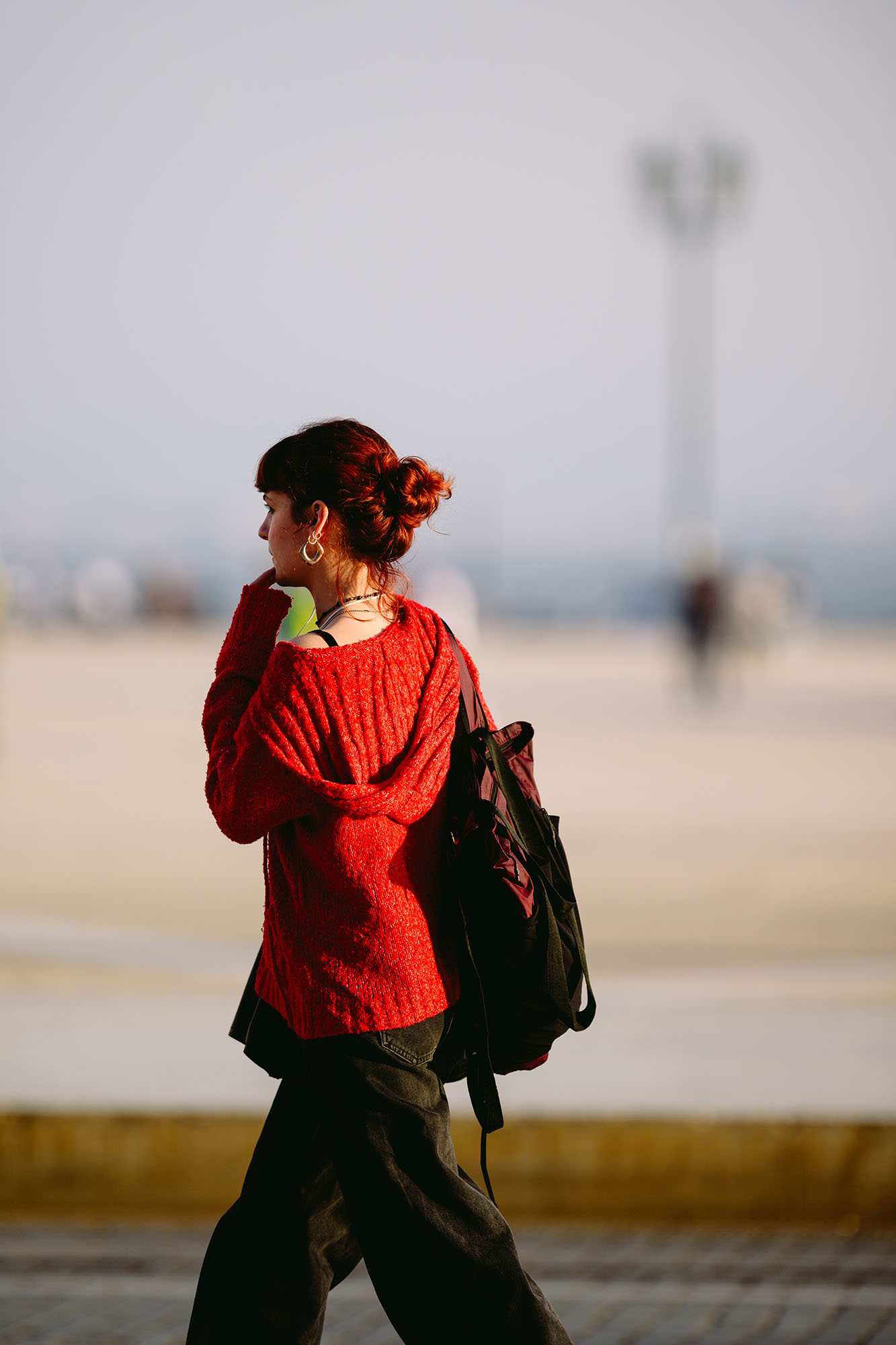 Woman with red hair and in a red sweater in the evening sun at the Praca do Comercio in central Lisbon, Portugal
